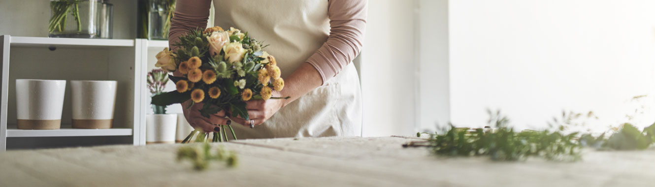 A woman's hands are tieing a bouquet of flowers together.